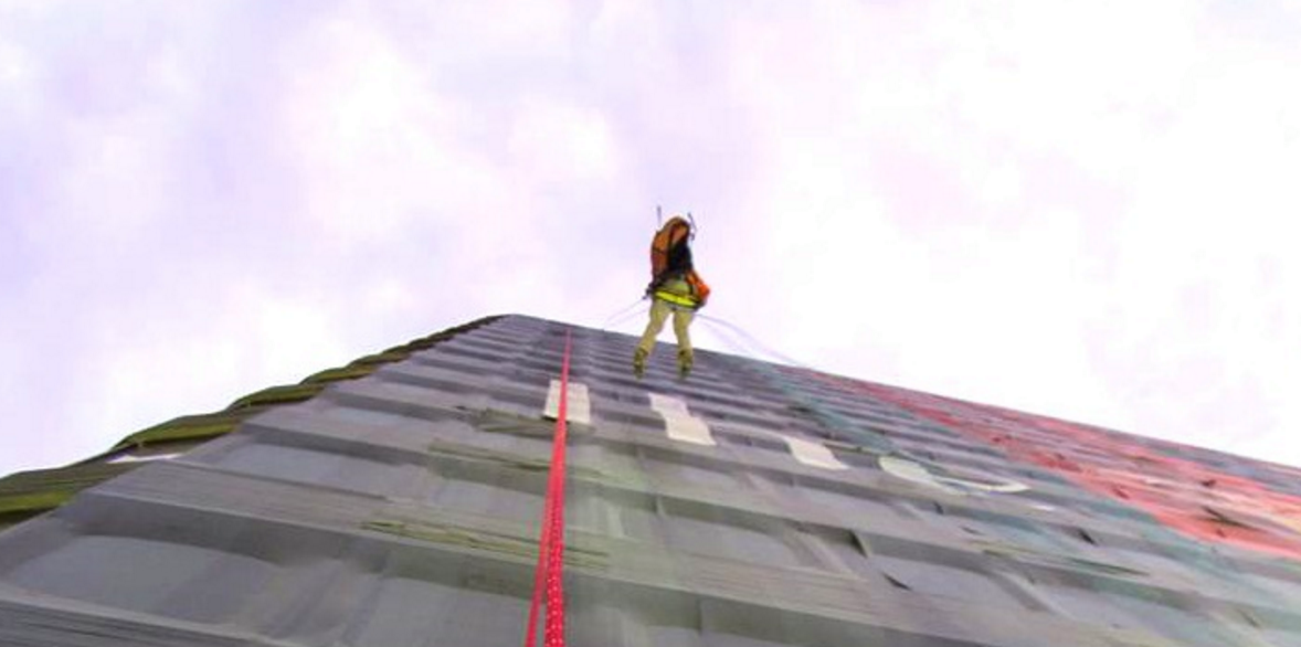 person rappelling down a building with a large format banner